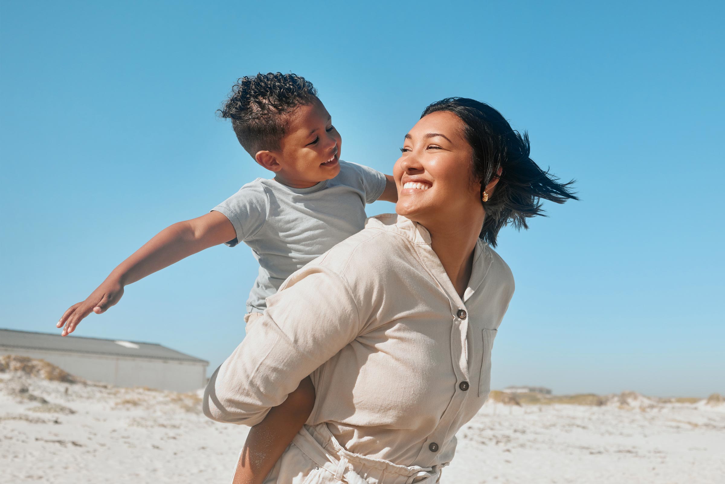 A mom carries her son on her back at the beach